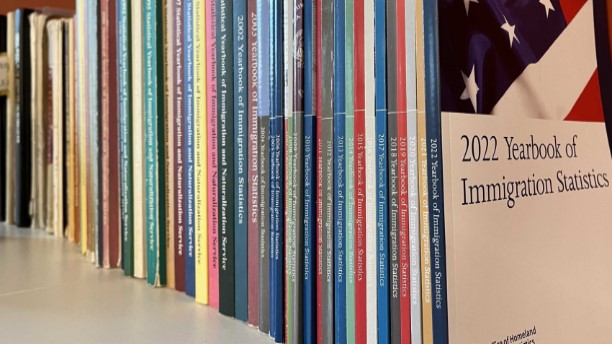 Many years of Yearbook of Immigration Statistics books on a bookshelf. The 2022 yearbook cover is visible at the end of the row.